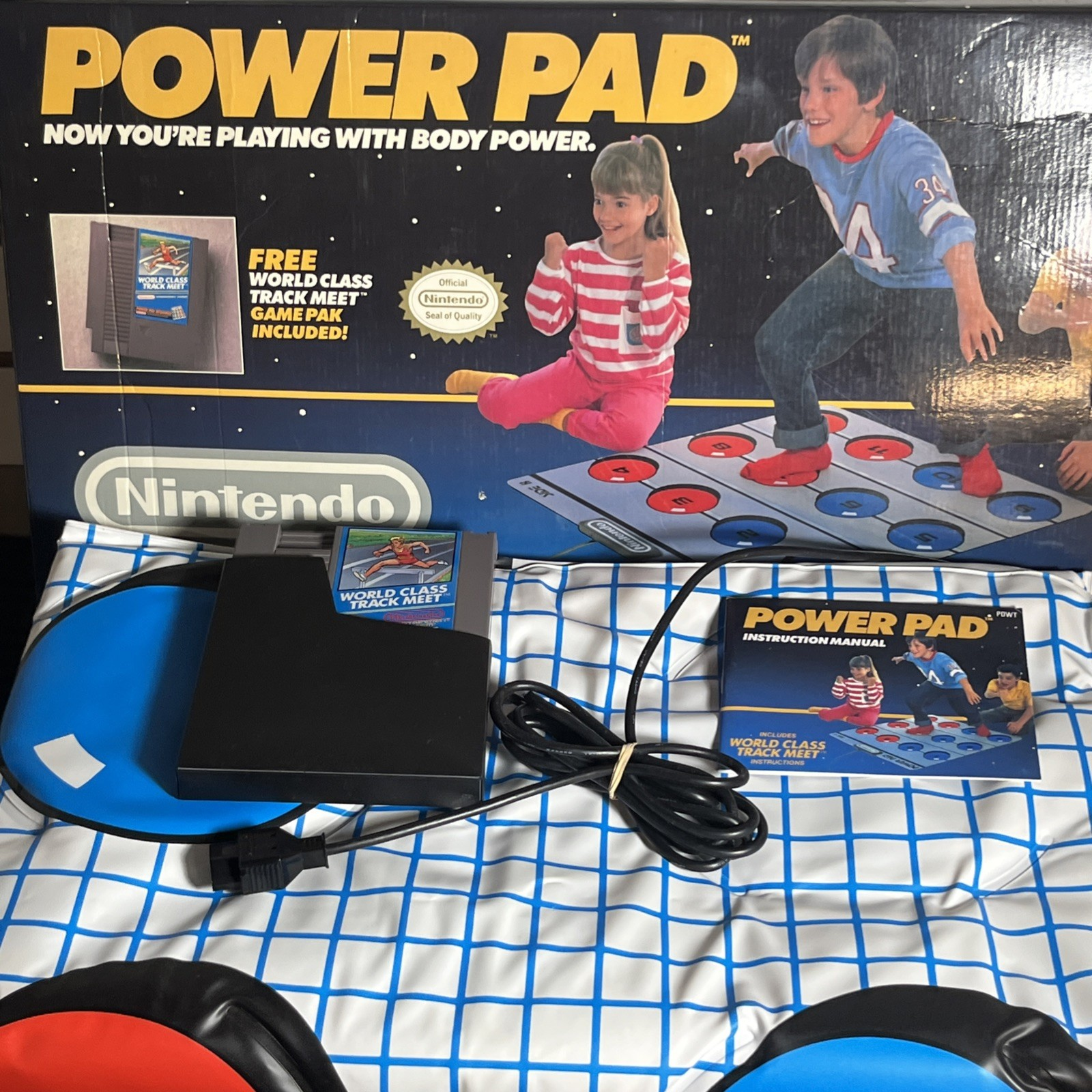 Nintendo Power Pad, eine Matte, dem Spielmodul und der Anleitung auf einem Bett.